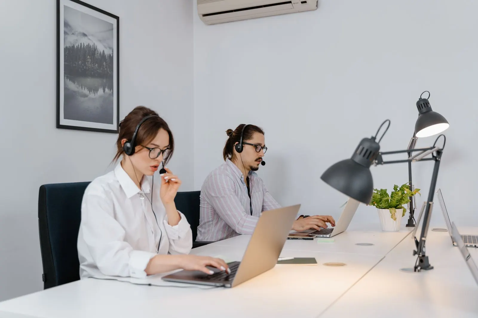 Two customer support agents with headsets working on laptops